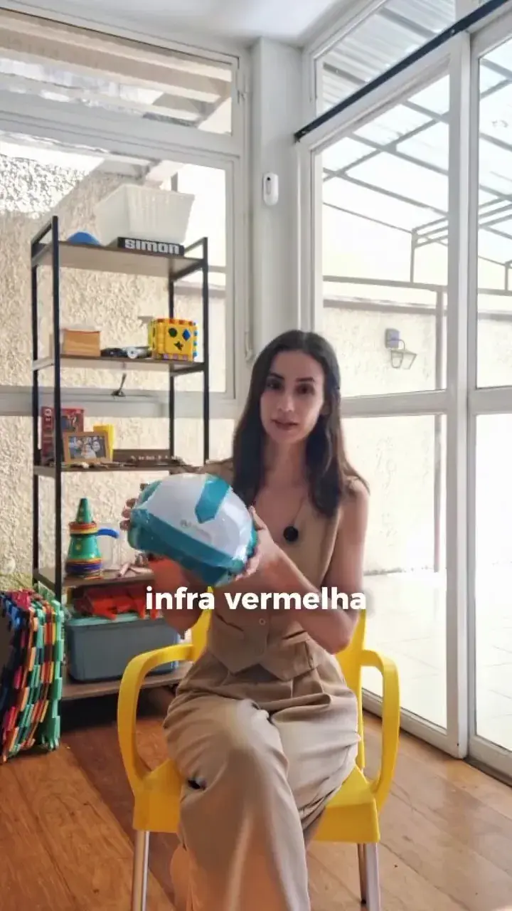 Profissional segura um capacete de fotoneuromodulação diante da câmera. A legenda na tela diz “infra vermelha”.