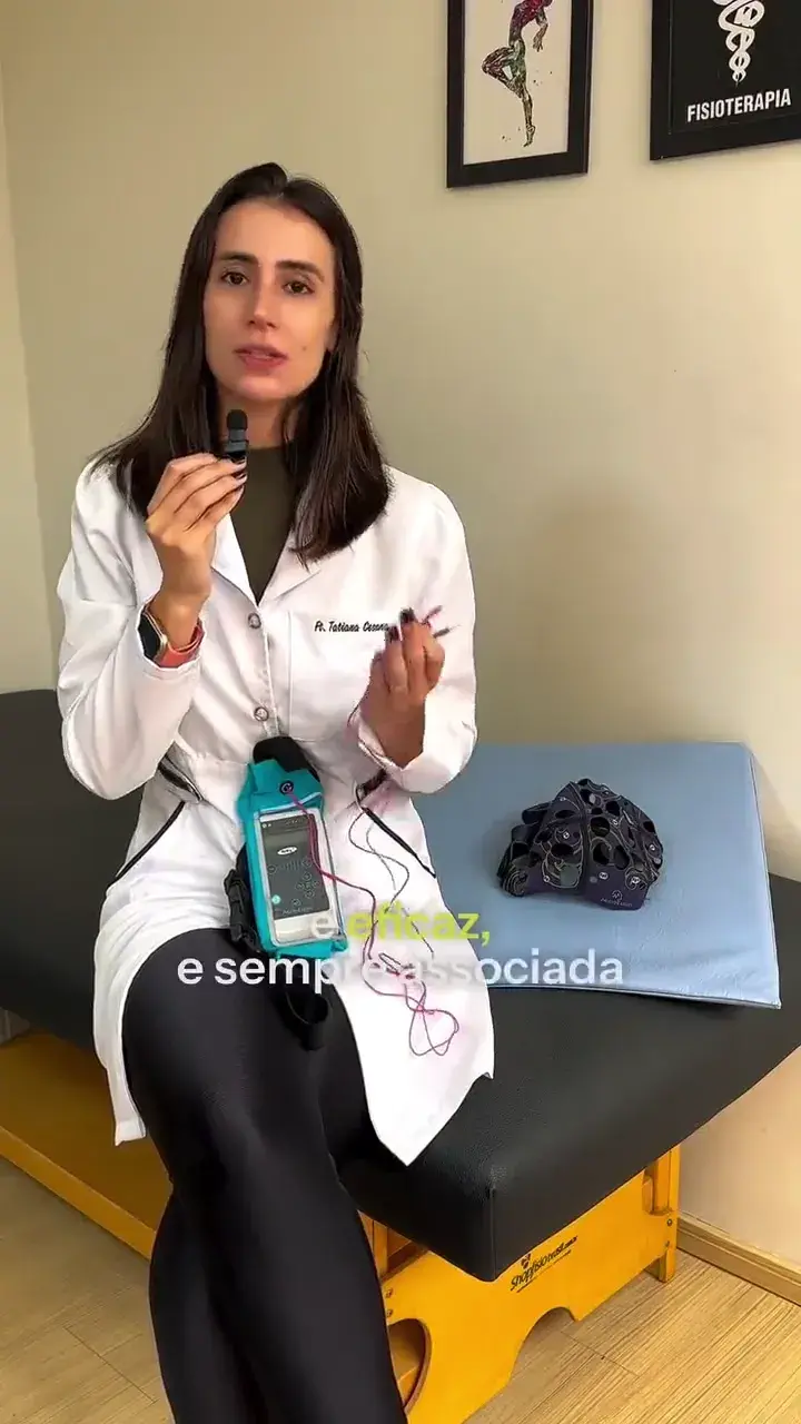 Profissional de jaleco branco sentada em uma maca, segurando o aparelho de neuromodulação, com a touca de eletrodos ao lado.